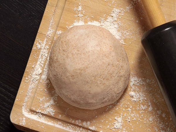 A dough ball on a cutting board with a rolling pin.