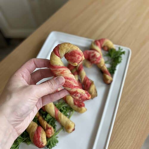 A person holding up a plate of twisted candy cane breadsticks.