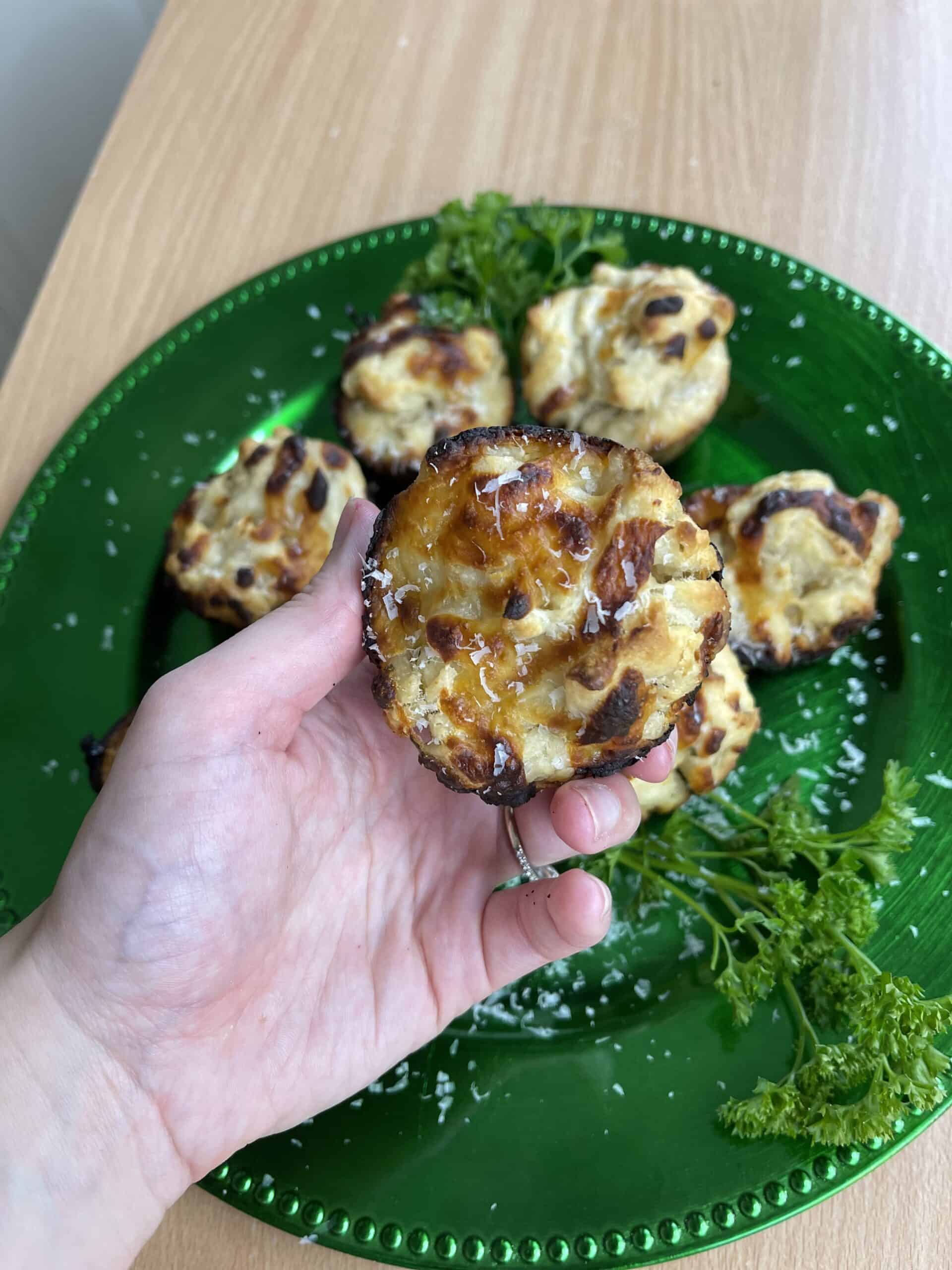 A person is holding a plate of mini cheesy muffin rolls on a green plate.