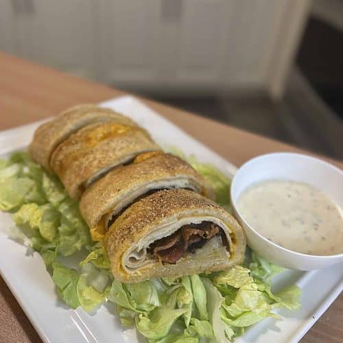 A chicken bacon ranch Stromboli with lettuce and dressing on a plate.