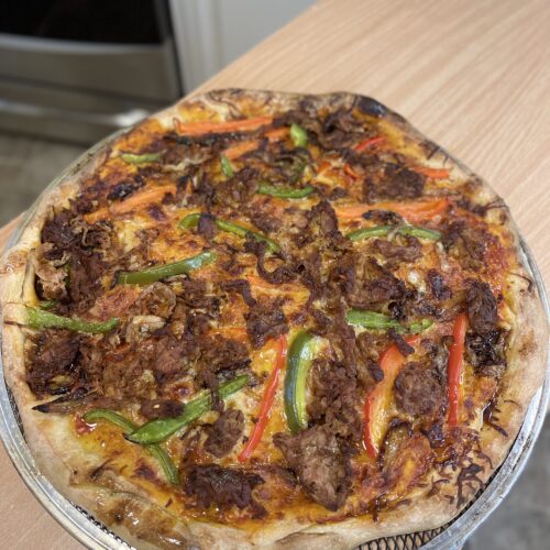 A pizza with meat and peppers on top of a metal pan.