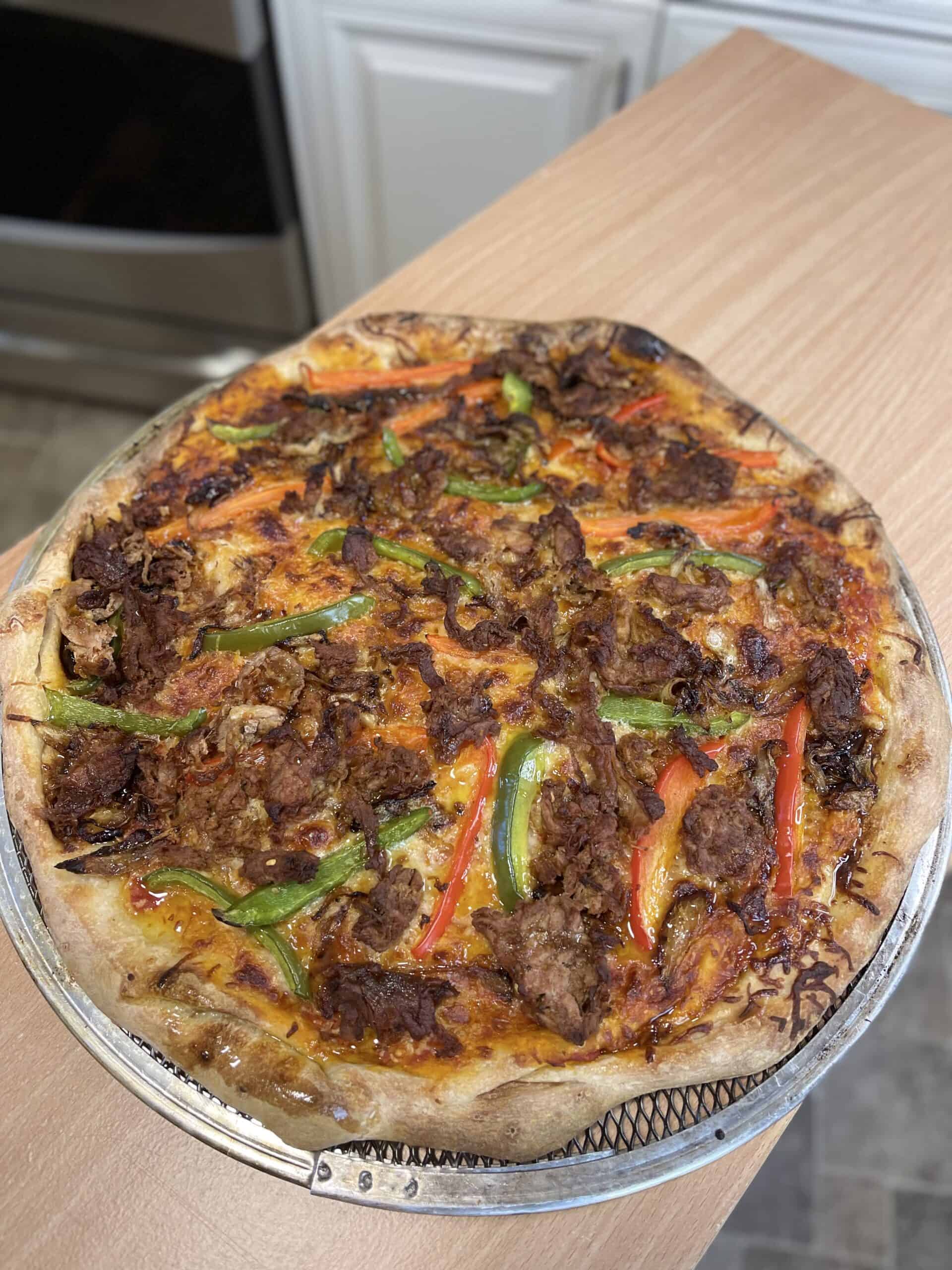 A pizza with meat and peppers on top of a metal pan.