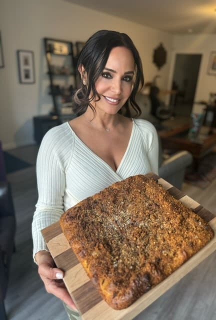 A woman smiling while holding a tray with a freshly baked cake.