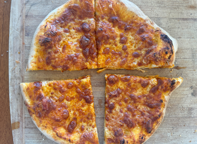 A cheese pizza made with authentic NY pizza dough is cut into four slices and placed on a wooden cutting board.