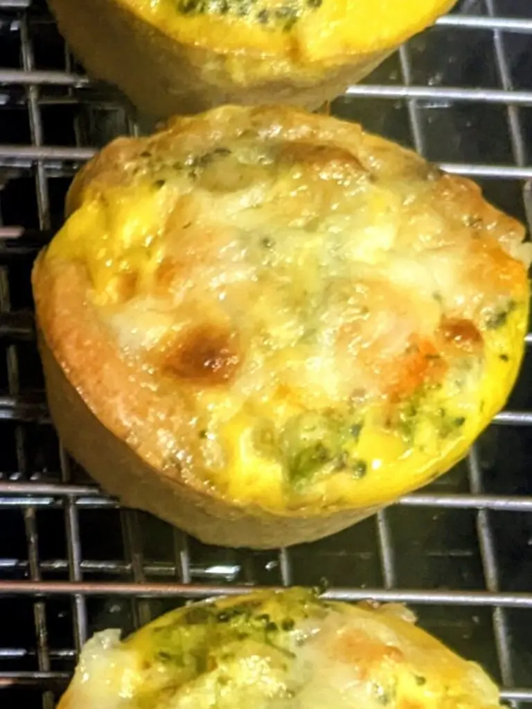 Close-up of a baked breakfast cup showing the golden pizza dough crust, melted cheese and broccoli.