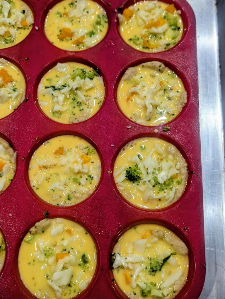 Pizza dough cups in a muffin pan filled with butternut squash, broccoli, whisked egg and shredded cheese, ready for the oven.