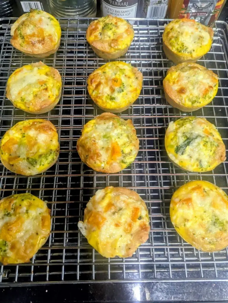 Twelve high protein breakfast cups made with Birrittella's protein rich pizza dough, filled with egg, butternut squash, broccoli and melted cheese, cooling on a wire rack.
